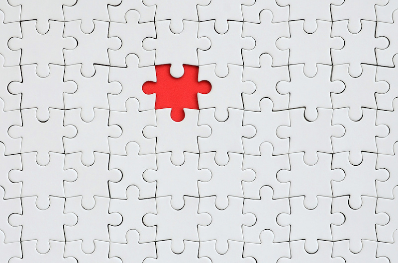 The texture of a white jigsaw puzzle in an assembled state with one missing element forming a red space