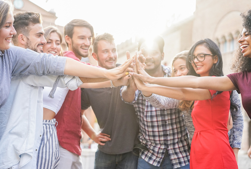 Young students stacking hands outdoor in college campus - Happy people celebrating together - Youth, university, relationship and friendship concept - Focus on hands - Original light color tones