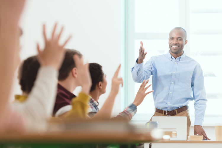 Smiling teacher and schoolchildren with arms up in classroom