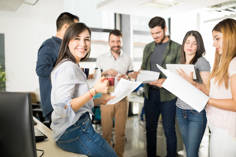 Portrait of young woman standing with colleagues reading some documents in office. Business people in office reading their contract papers.