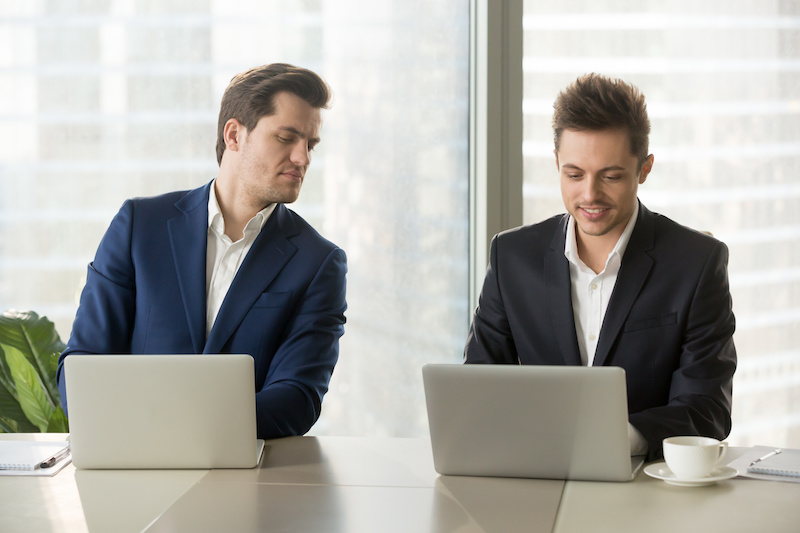 Curious businessman secretly looking at laptop screen of colleague, sneaking peek at other computer, stealing idea, copying private information on exam, nosy clerk spying on coworker at workplace