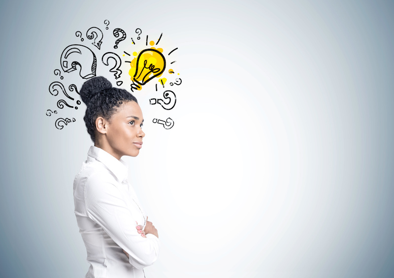 Portrait of a strong and independent woman wearing a white shirt and standing with crossed arms near a gray wall with a small light bulb and question marks. Mock up