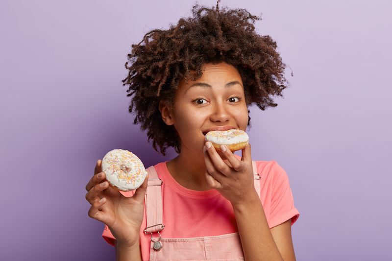 Hungry woman bites tasty doughnut with bright sprinkles
